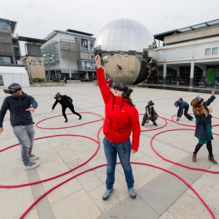 Photo of people wearing VR headsets in Bristol's Millenium Square taking part in Dancing Shadows