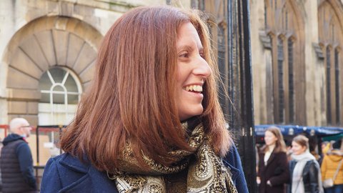 Head and body shot of Charlotte Lester, Watershed Board member, smiling, with red long hair, wearing a blue coat and a patterned scarf.