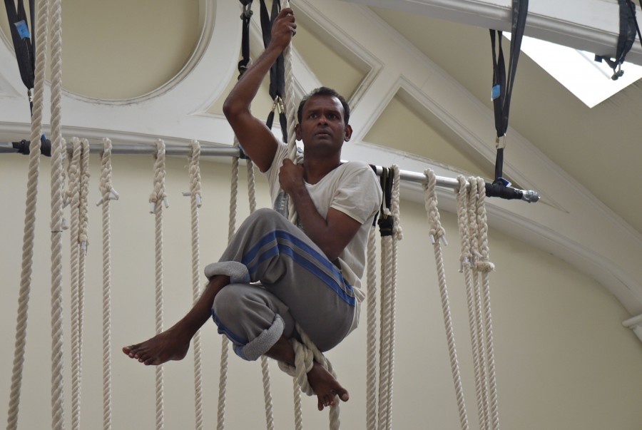 Ramesh Mayyappan up a rope - he is sitting holding the rope with his legs crossed in front of him.