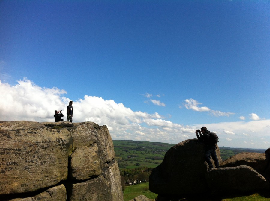 A huge rocky outcrop against a blue sky - two figures can be seen on one rock and another film maker can be seen in the foreground, also shooting