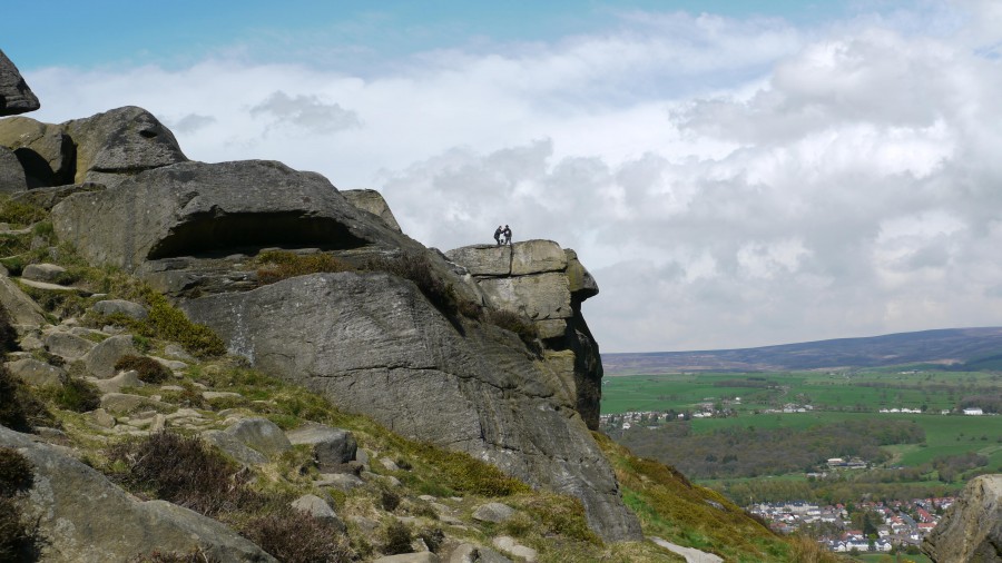 A huge rocky outcrop against a cloudy sky - two tiny figures can be seen - one filming, one in a stetson.