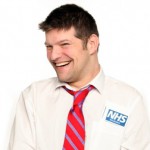 a head and shoulders shot of Laurence Clark - he is in a white shirt and red tie with an NHS badge on. He is smiling cheekily.