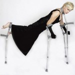 Claire Cunningham balancing on four crutches - two for her arms, one for her legs and one at her neck. She is all in black including with black long gloves.