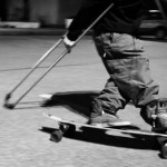 the bottom half of a man, feet on a skateboard, with crutches being used to propel the figure forwards