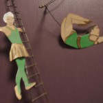 two circus figures - one on a ladder and one on a trapeze - they are made of flat metal and part of a wall hanging