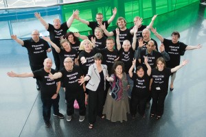 a group of about 20 people, shot from above, all with their arms in the air (and all wearing black 'streetwise choir' tshirts)