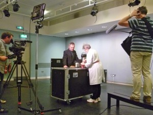 Charles having tea with Bobby Baker using one of her flight cases from her show as a table. - you can see the cameras filming them.