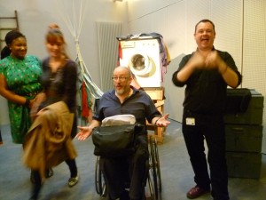 Tony Heaton from shape in the centre, with an animated sign language interpreter to his right and some women on the tour to his left.