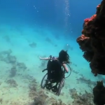 screen shot of Sue Austin diving underwater in her underwater wheelchair.