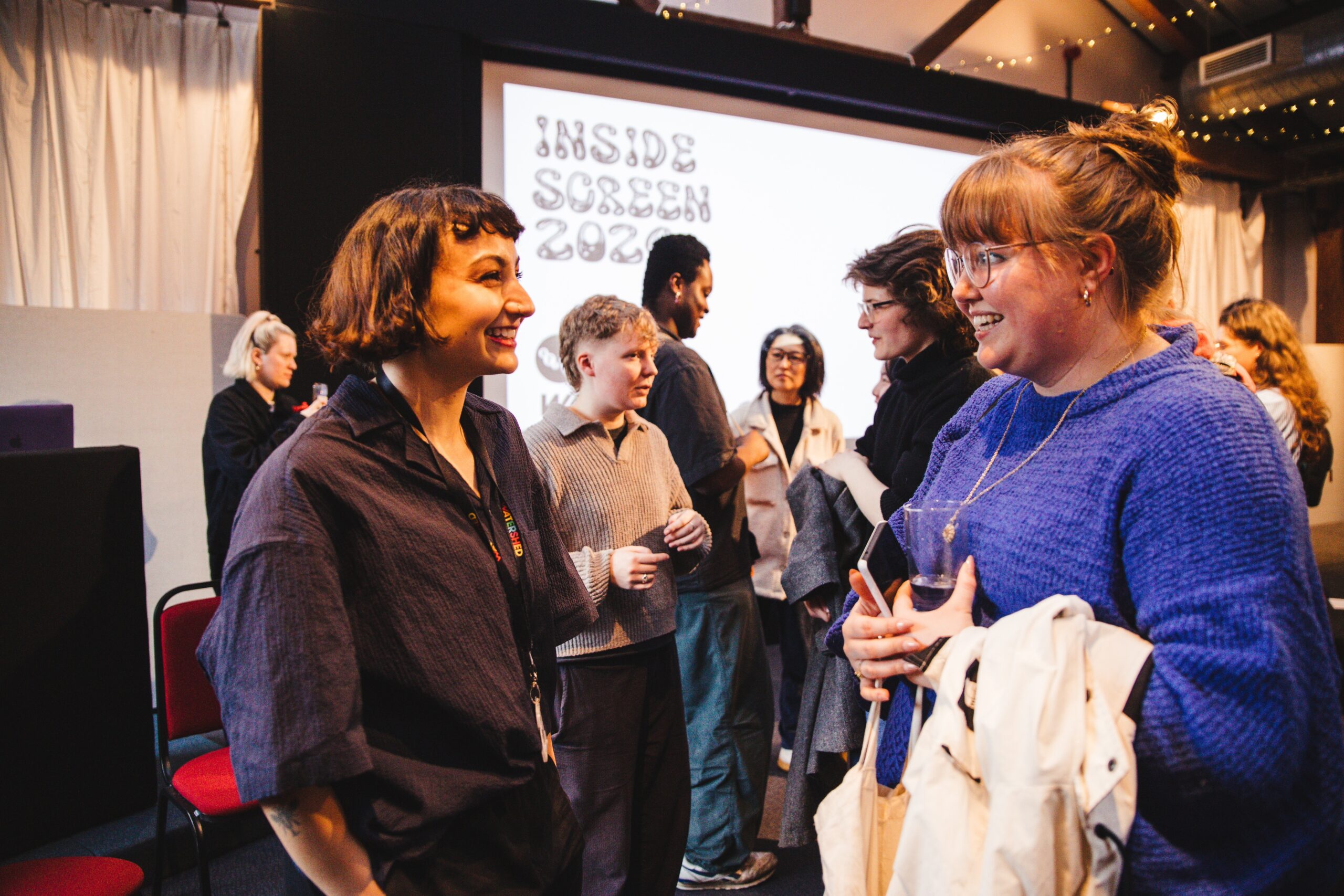 A group of attendees networking at Inside Screen 2024. Two women at the front are smiling and chatting to each other.