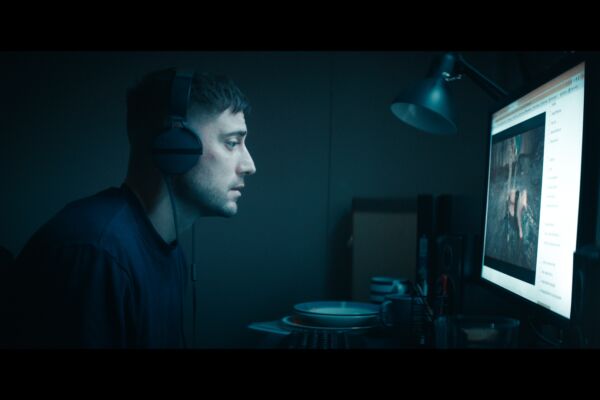 a white man with headphones on stares at a computer screen in the dark