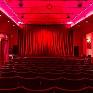 Inside a cinema auditorium, plush space with red lighting, chairs, and curtain