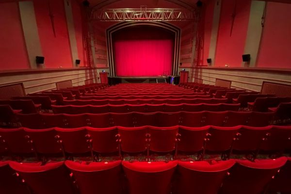 An empty cinema, shot taken as though seated at the back looking over rows of chairs to a red screen. All seats and walls are red giving warm glow to the low lighting