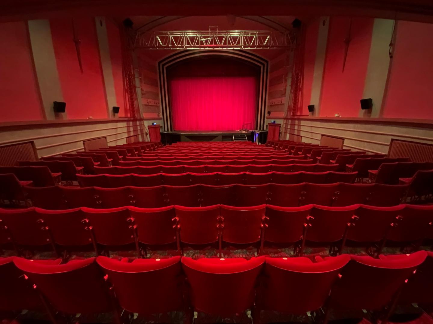 An empty cinema, shot taken as though seated at the back looking over rows of chairs to a red screen. All seats and walls are red giving warm glow to the low lighting