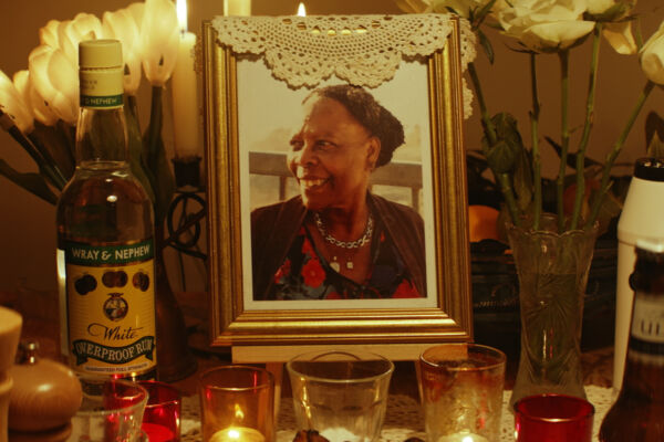 a shrine to a woman at her nine nights. a warmly lit table with candles has a gold framed photo, bottle of rum