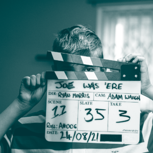 image of a young boy looking through a clapper board. the image is duotone blue hues.