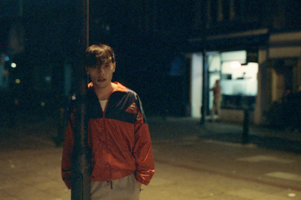 a boy looms next to a lamppost. he is illuminated, looking pale in its orange glow on a dark night