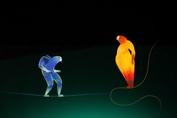 Two hand drawn paper creatures look towards each other inquisitively. on the left, the blue creature llooks like a llama or a bear. soft and blobby and friendly. On the right, the character is identical, only orange. the background is a plain deep green, and the figures stand on a short piece of string, as if balancing across a night sky