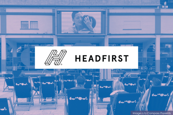 headfirst logo, overlaid on a duotone image. decorative graphic image. the image behind is of people sat on deckchairs, watching a film. we see the back of them and the film plays on a screen up on a building.