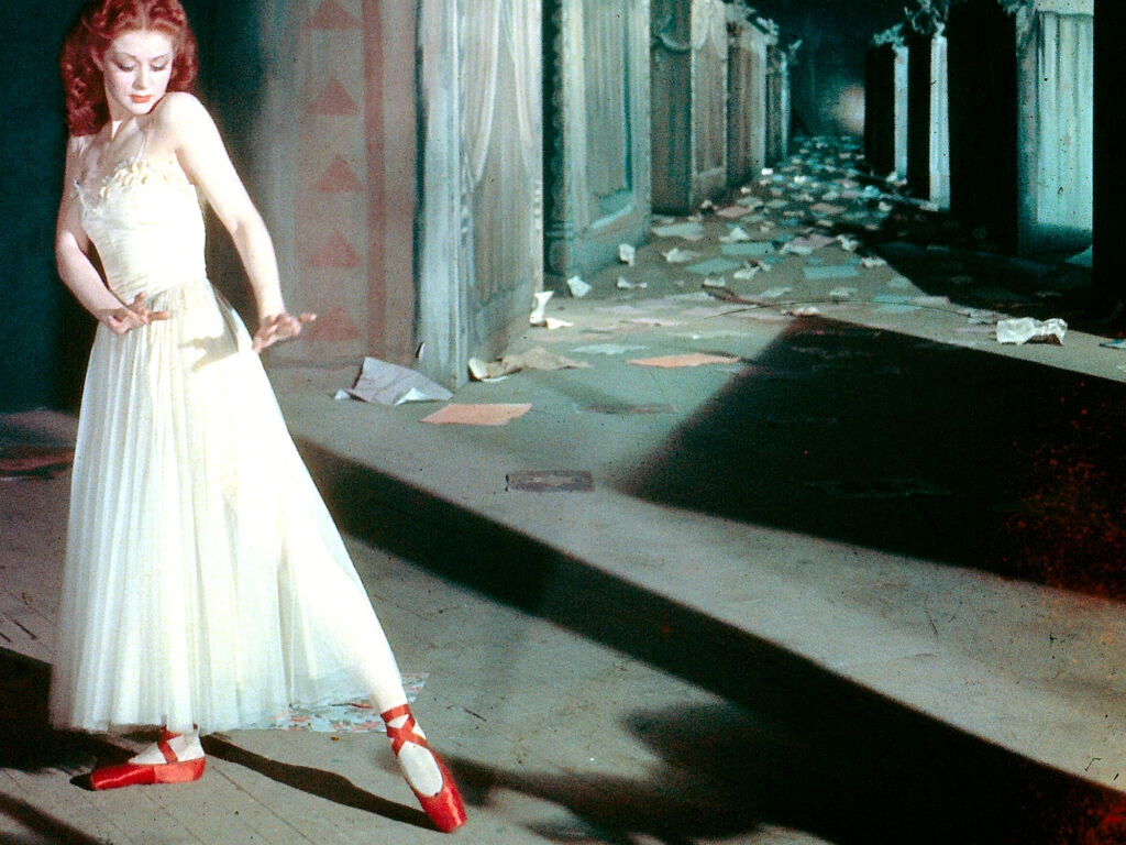 A still from Red Shoes with a ballet dancer striking a pose looking at her striking red shoes.