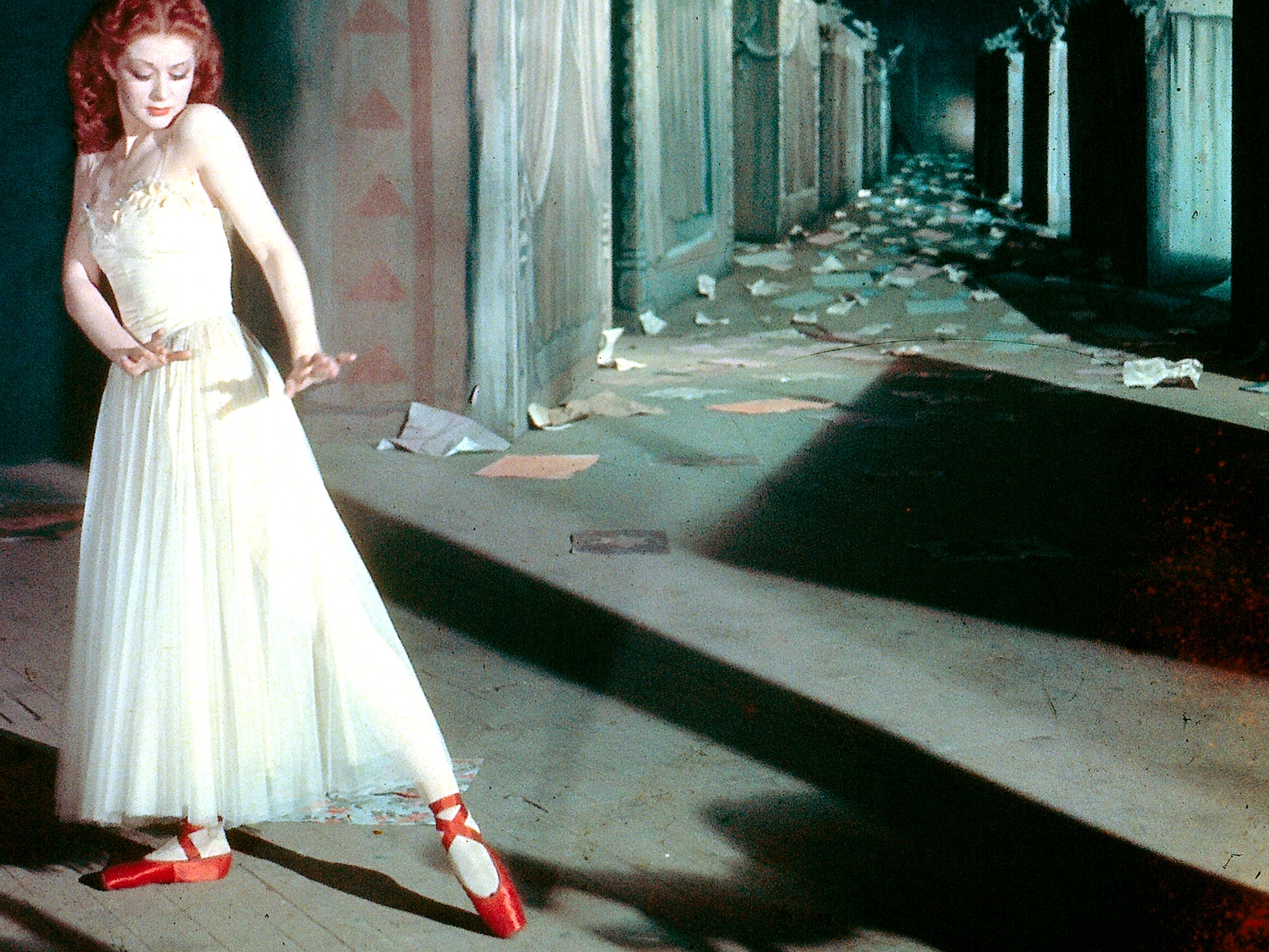 A still from Red Shoes with a ballet dancer striking a pose looking at her striking red shoes.