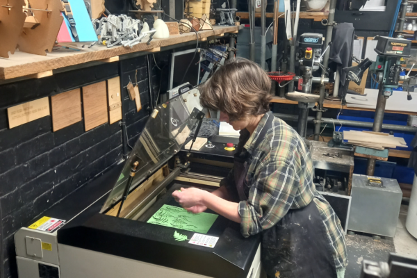 a person operating a laser cutter in a bustling creative studio