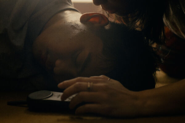 close up of a mans head on the floor. in dark room , a woman leans over him