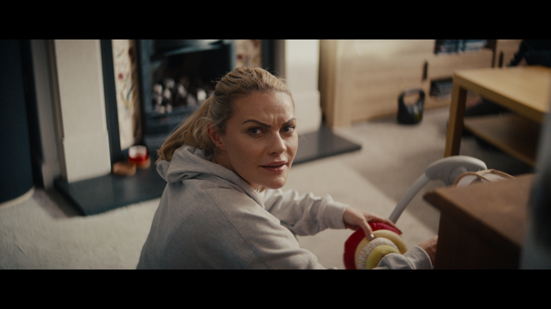 A mid shot of a white woman looking with a confused expression behind the camera, while sat on the floor of a living room