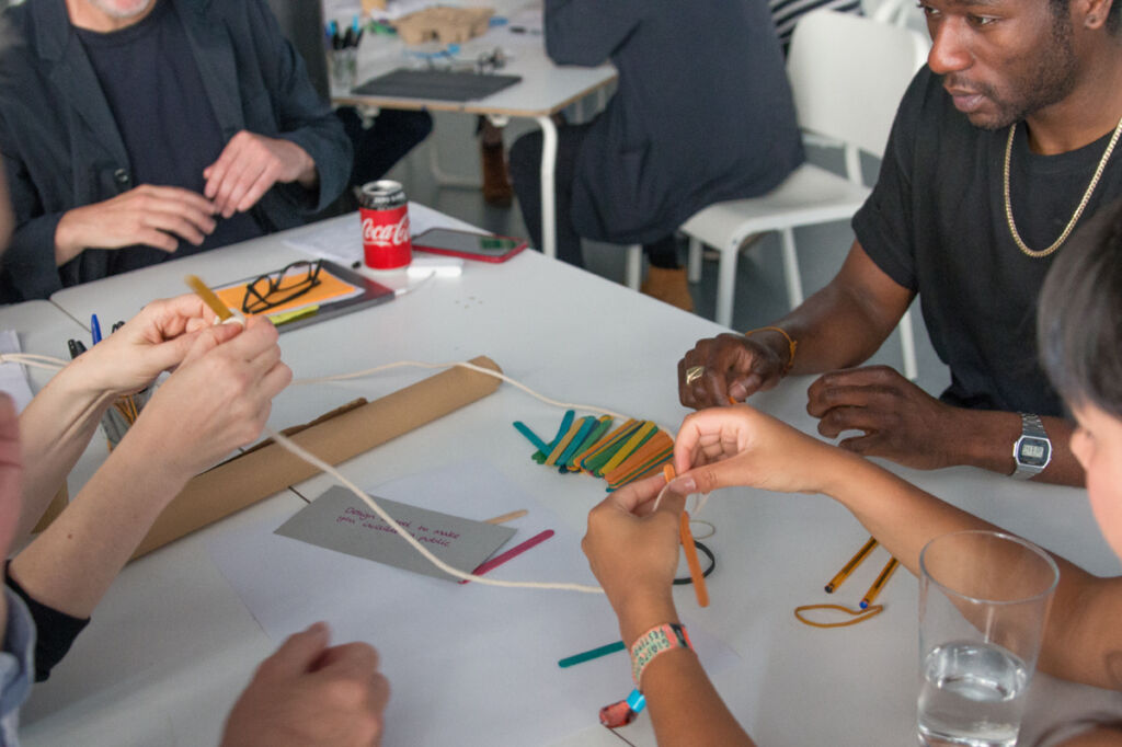Photo of people working together around a table making things with string and lollipop sticks and more