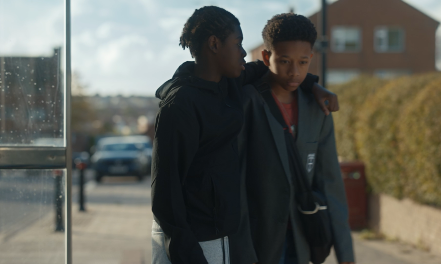 Two young boys walk closely together on a sidewalk, one with an arm around the other's shoulder, evoking a sense of solidarity and companionship.