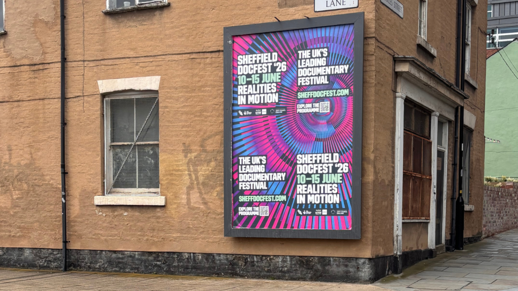 A billboard for Sheffield DocFest '26 is featured on the exterior of a brown brick building.
