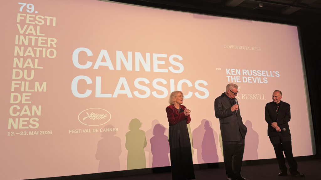 Three people dressed in black stand on stage in front of a large cinema screen reading: Cannes Classics