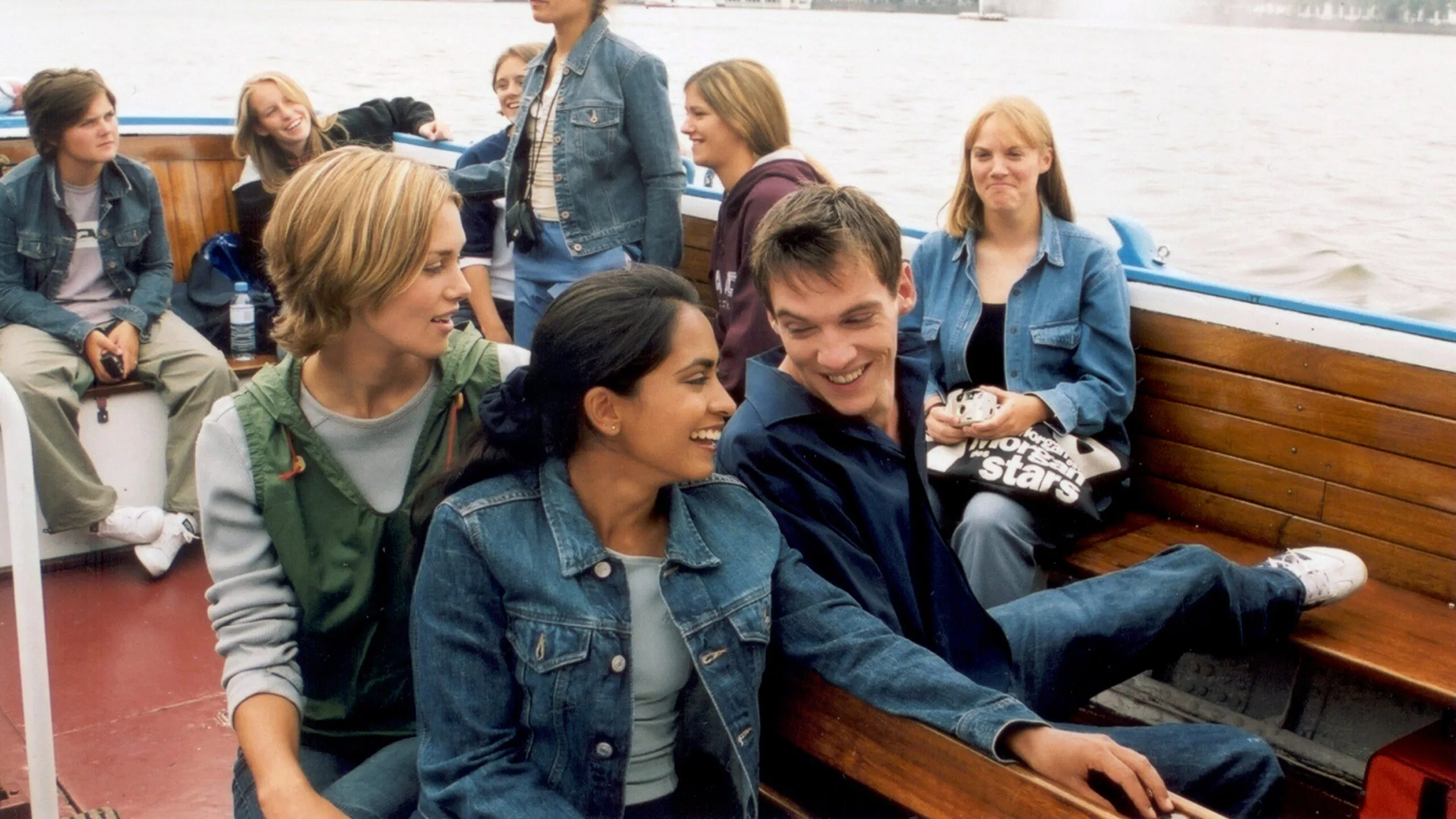Group of young people smiling on a boat, seated by the river.
