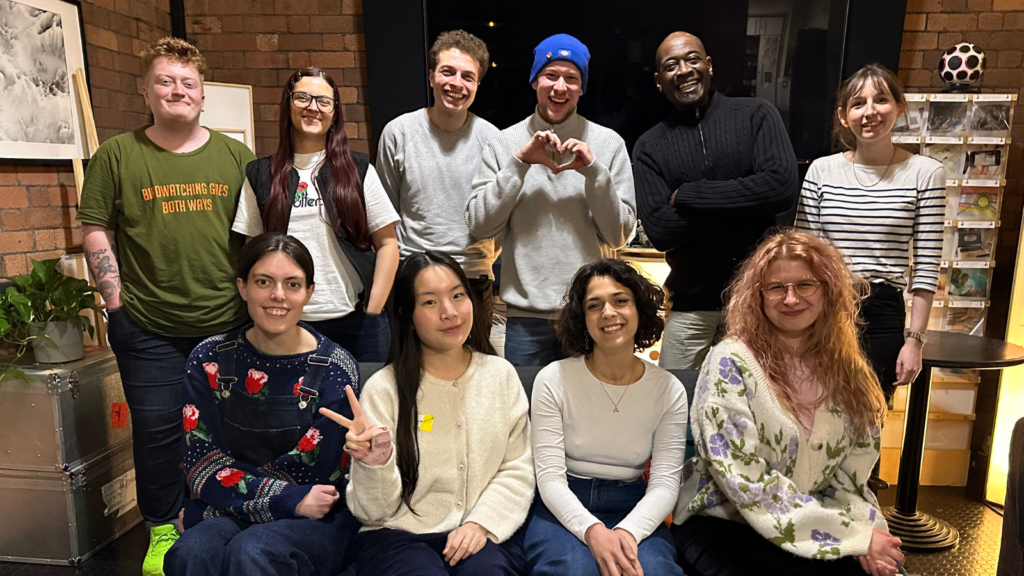 Ten people pose together and smile in front of a wall.