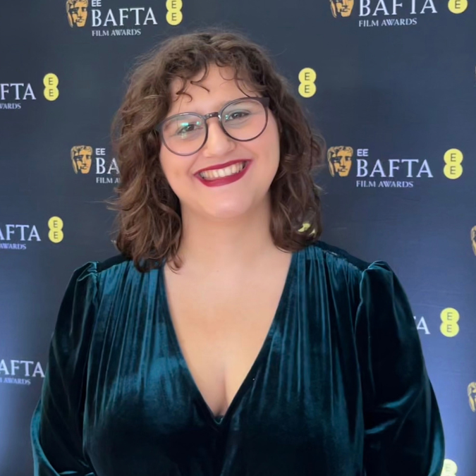 A woman smiling in front of a BAFTA step and repeat.