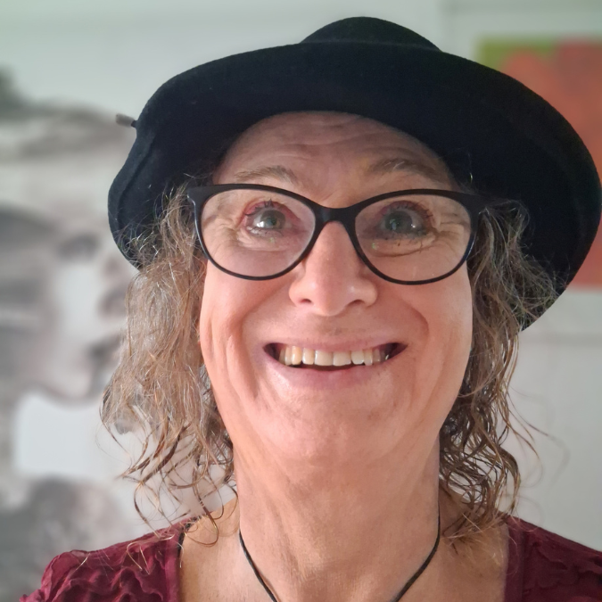 A selfie of a smiling woman with glasses and a black hat on.