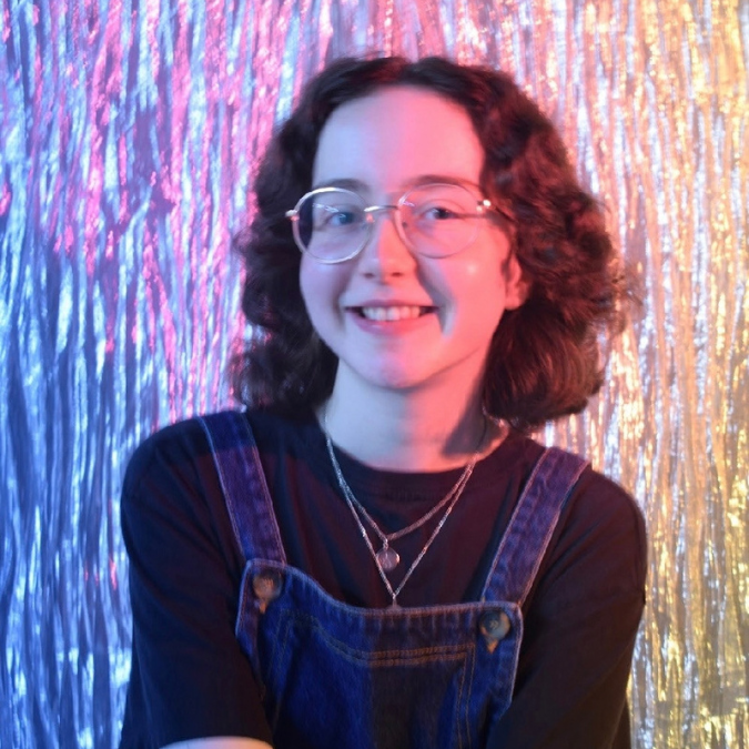 A woman with glasses smiling in front of colourful streamers.