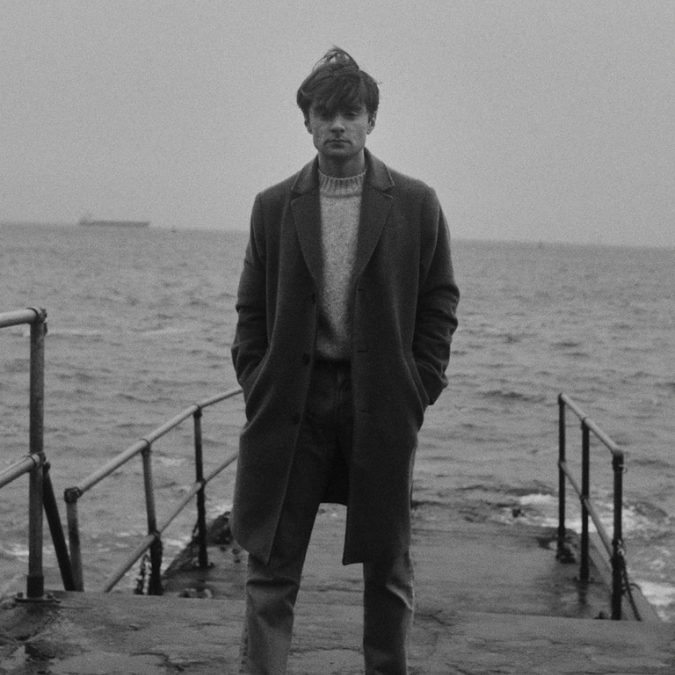 A black and white photo of a man standing on a pier.