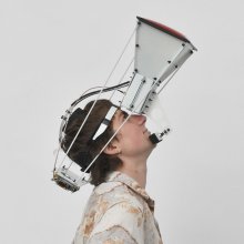 A person wearing a large projector-like device strapped to their face, gazes up.