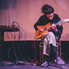 A man sits on a stool, playing a guitar.