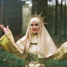 A woman dressed as a golden Virgin Mary poses in a forest.