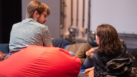 Three people sitting and lying down resting. One on a bean bag and two on cushions.