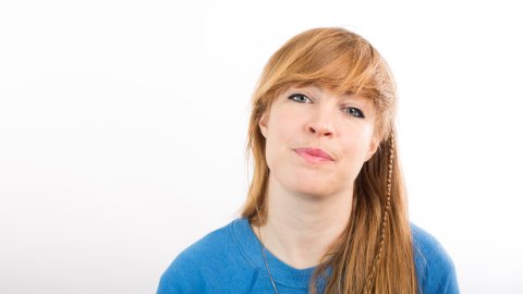 Photo of a white woman with long hair, looking straight at the camera and wearing a blue jumper