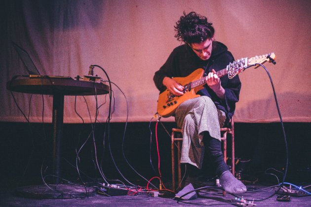 A man sits on a stool, playing a guitar.